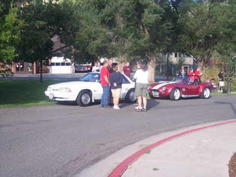 1972 Ford Ranchero - People gather around a white 1987 Ford Mustang and a red Cobra replica during an outdoor event.
