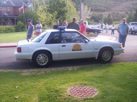1972 Ford Ranchero - A white patrol car with a light bar on top is parked on the grass, with several people standing nearby.