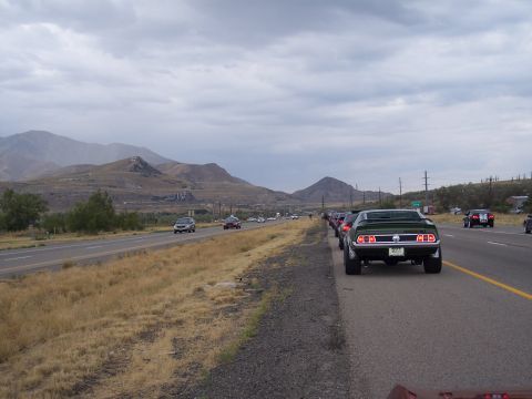 1972 Ford Ranchero - A convoy of classic cars travels down a highway with mountains in the background under a cloudy sky.
