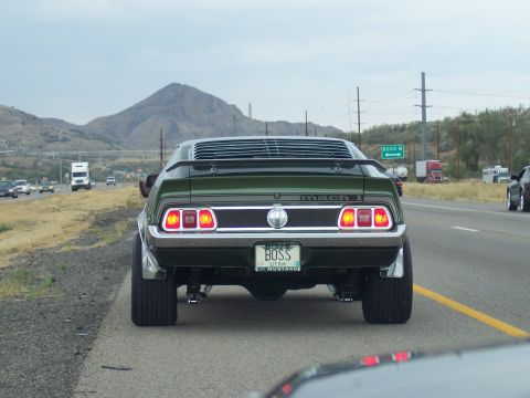 1972 Ford Ranchero - A green 1973 Ford Mustang Mach 1 with a custom 'BOSS' license plate is seen from behind on a highway.