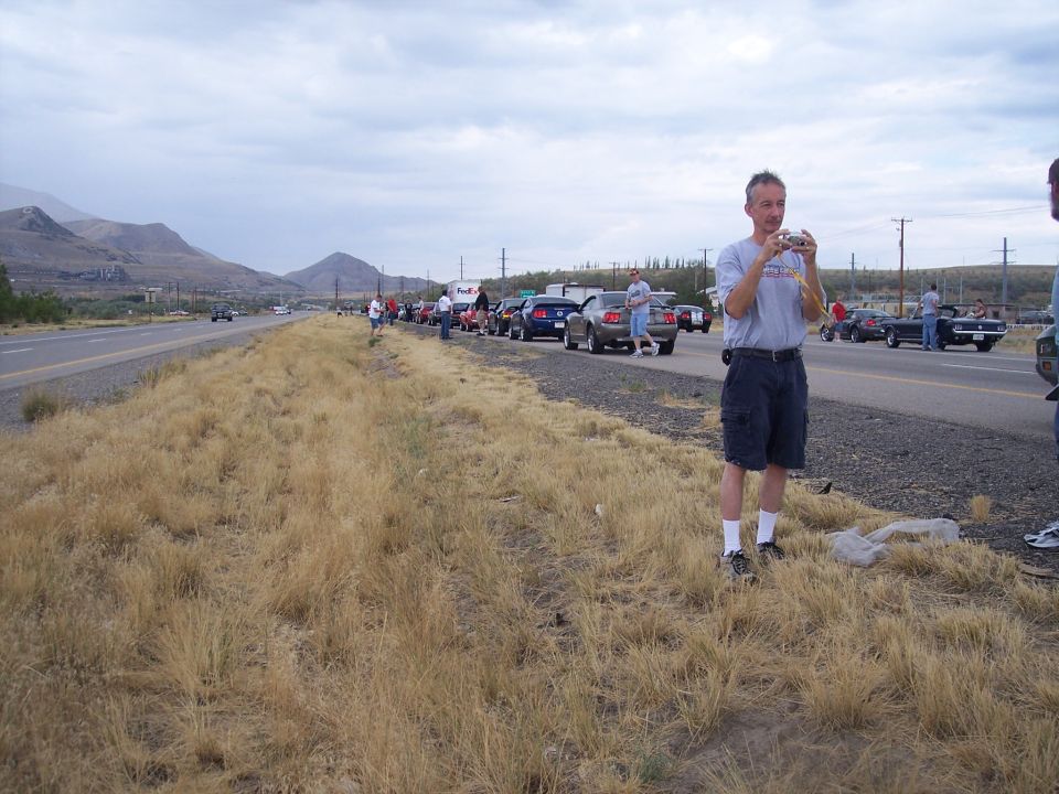 Man with camera on highway median with line of parked cars behind him