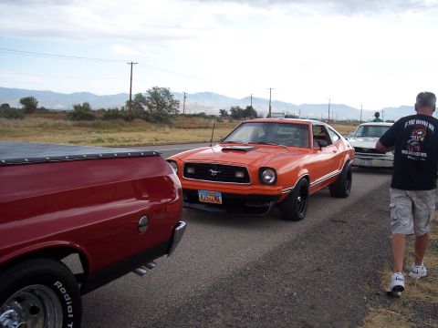 1972 Ford Ranchero - An orange 1977 Ford Ranchero is seen from the front-three-quarter view, parked behind a red pickup truck.