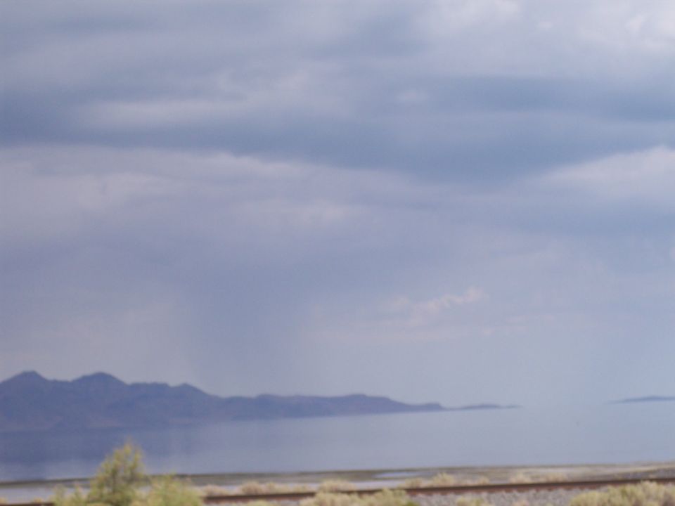 Distant mountains beside a lake under gray clouds with railroad tracks in foreground