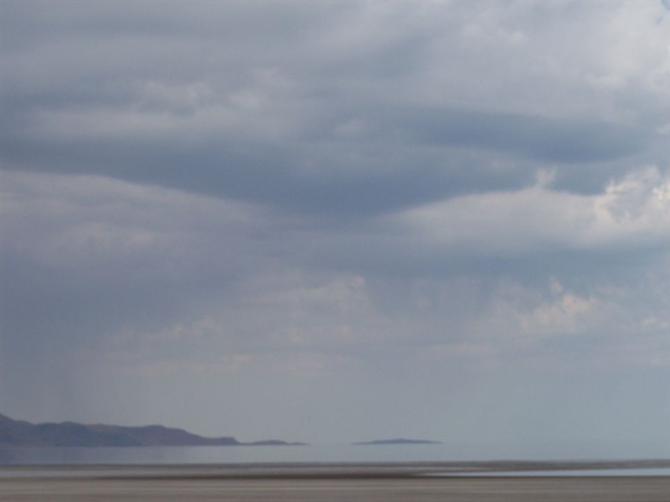 Overcast sky over calm water with distant hills on the horizon