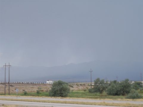 1972 Ford Ranchero - A white truck travels down a highway, dwarfed by the vast, overcast sky and distant mountains.
