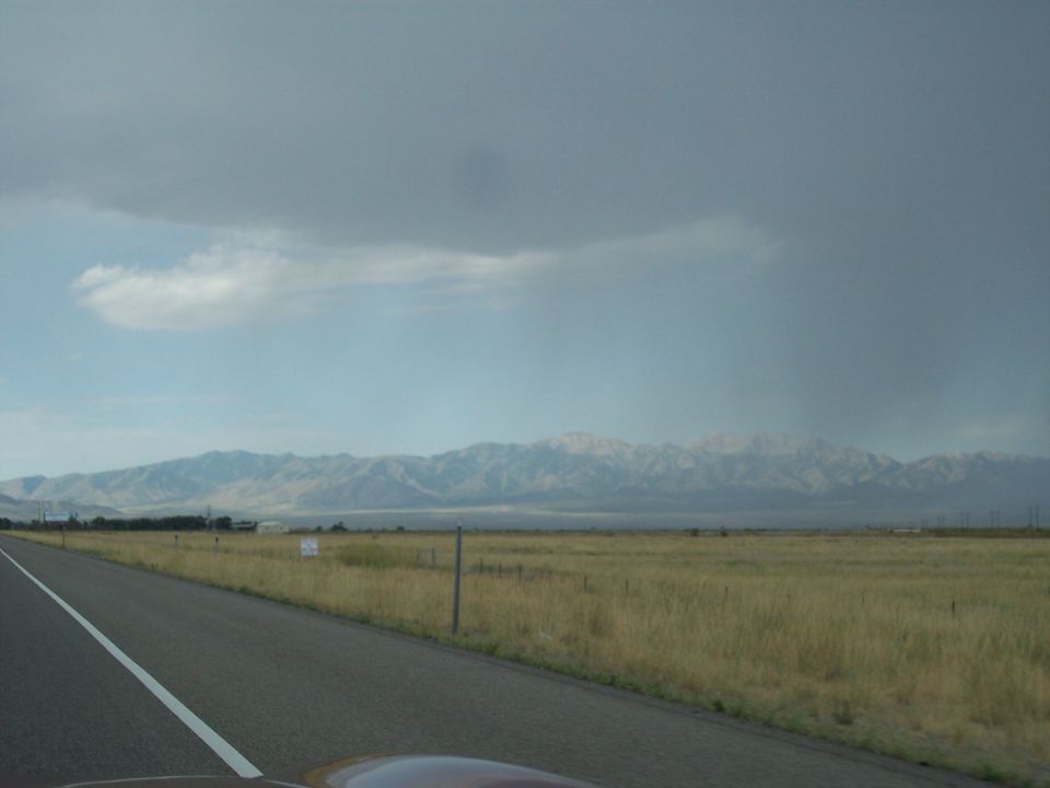 Highway shoulder with golden grassland and distant mountains under a stormy gray sky