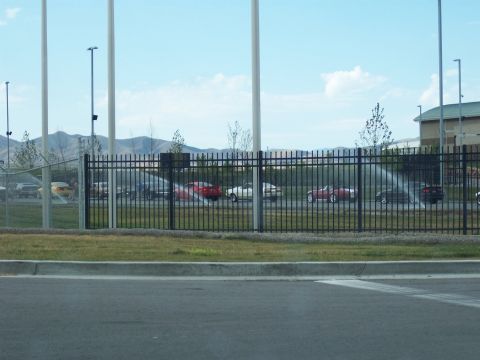 1972 Ford Ranchero - A variety of vehicles are visible behind a fence, with sprinklers watering the grass in front of them.