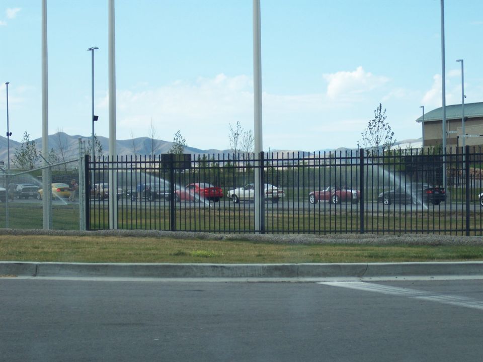 Parking lot with assorted cars seen through a black fence, mountains behind