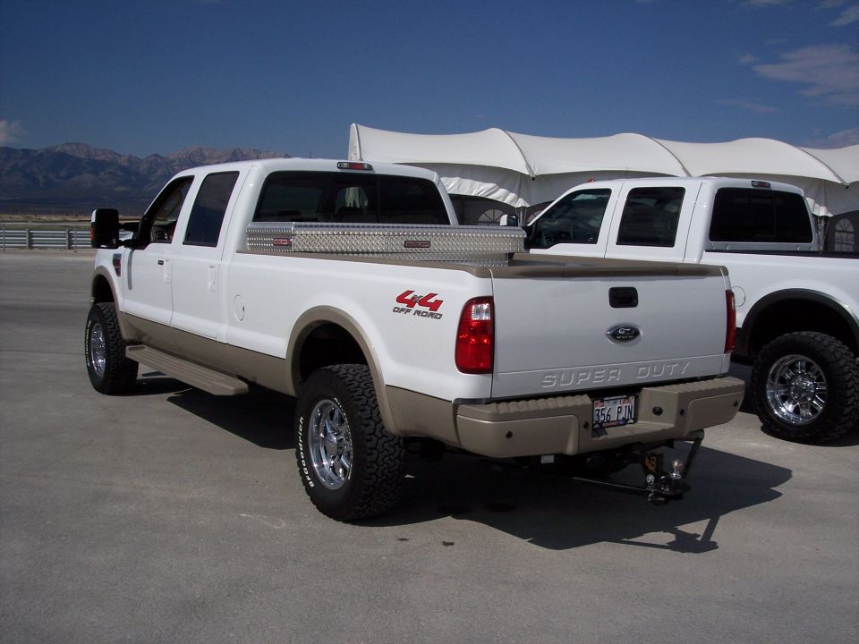 White Ford Super Duty 4x4 crew cab pickup, rear 3/4 view with bed toolbox