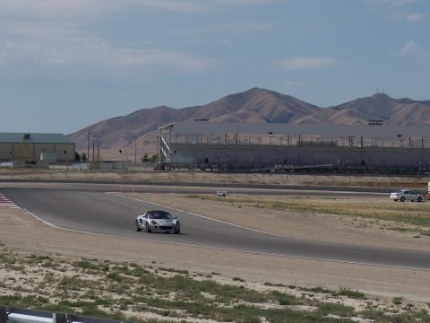 1972 Ford Ranchero - A silver sports car navigates a turn on a race track with a grandstand and mountains visible.
