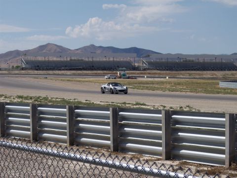 1972 Ford Ranchero - A silver sports car navigates a race track, with grandstands and distant mountains under a partly cloudy sky.