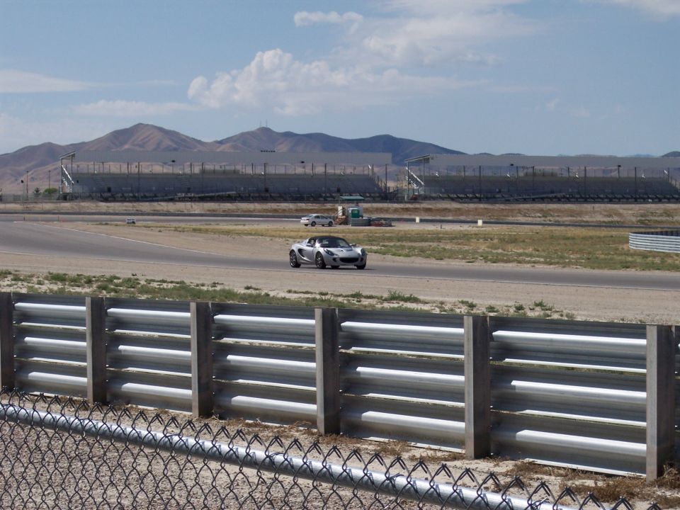 Silver sports car on a racetrack with grandstands and mountains behind
