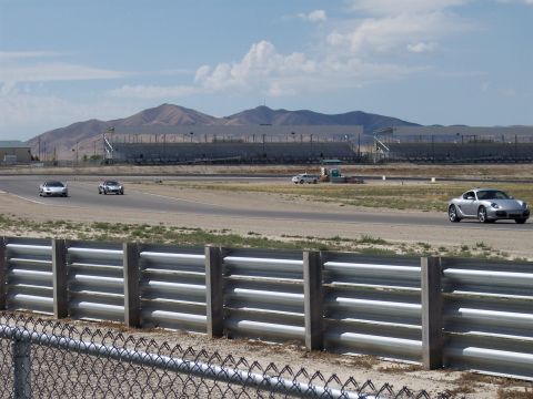 1972 Ford Ranchero - Sports cars navigate a race track under a partly cloudy sky, with distant mountains and grandstands visible.