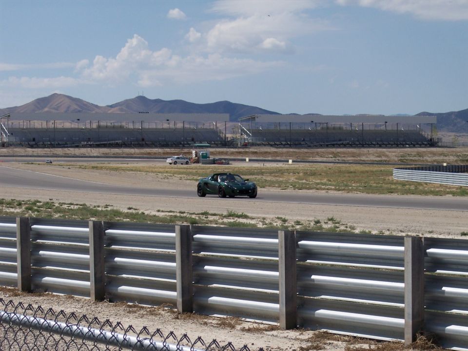Dark green sports car on a race track with grandstands and mountains behind