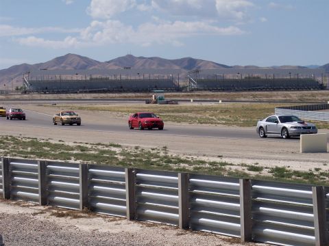 1972 Ford Ranchero - Several cars race on a track with grandstands and mountains in the distance.