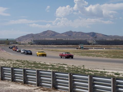 1972 Ford Ranchero - A red convertible leads a procession of cars on a racetrack with grandstands in the background.