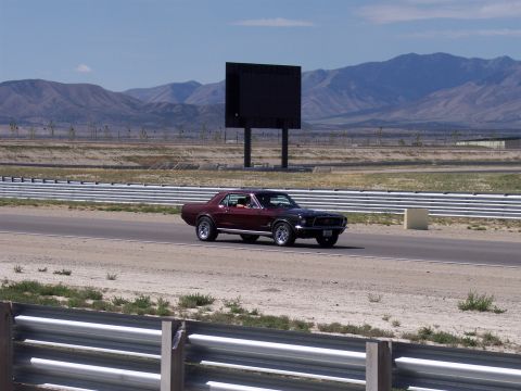 1972 Ford Ranchero - A maroon 1967 Ford Mustang coupe is seen on a racetrack under a clear sky.
