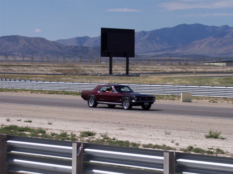 Maroon classic coupe driving on a track with mountains behind