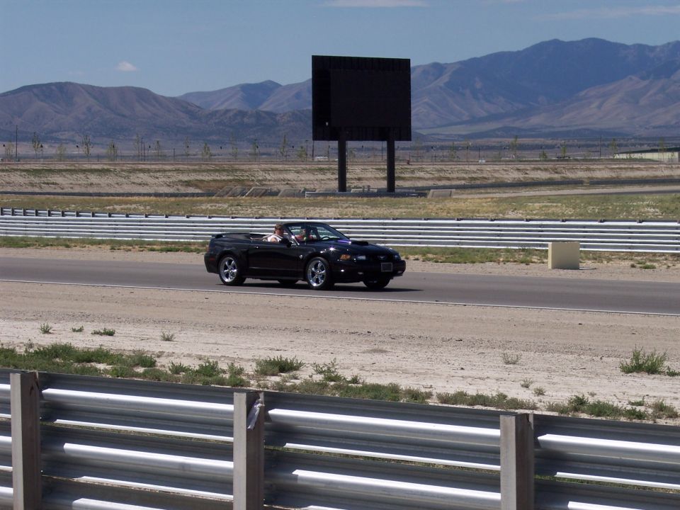Black convertible with top down on a racetrack with mountains behind