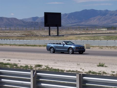 1972 Ford Ranchero - A blue convertible Mustang drives on a track, with mountains and a large screen in the distance.
