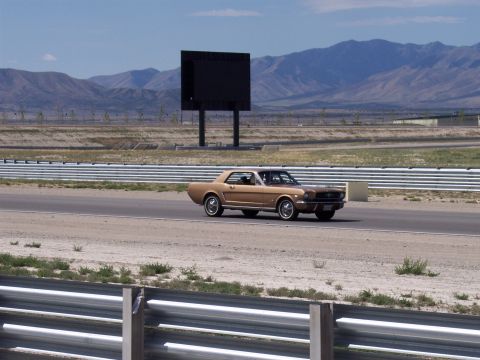 1972 Ford Ranchero - A classic brown Ford Mustang coupe drives on a paved track with mountains in the background.