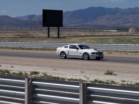 1972 Ford Ranchero - A white Ford Mustang drives on a racetrack with mountains in the background.