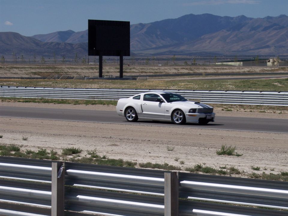 White coupe with dark racing stripe driving on a track with mountains behind