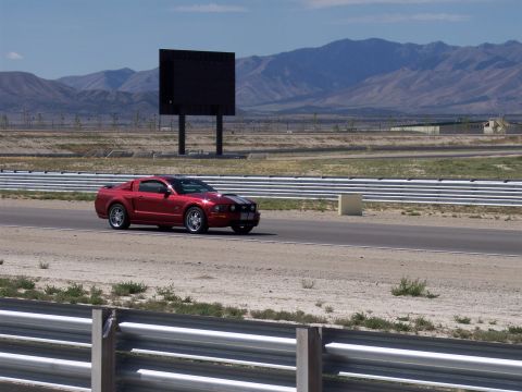 1972 Ford Ranchero - A red Ford Mustang drives on a race track with a large black screen in the background.