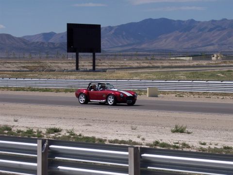 1972 Ford Ranchero - A red convertible speeds down a race track under a clear sky with mountains in the distance.