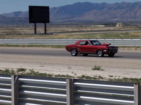 1972 Ford Ranchero - A red coupe with a hood scoop is captured in motion on a race track with mountains in the background.