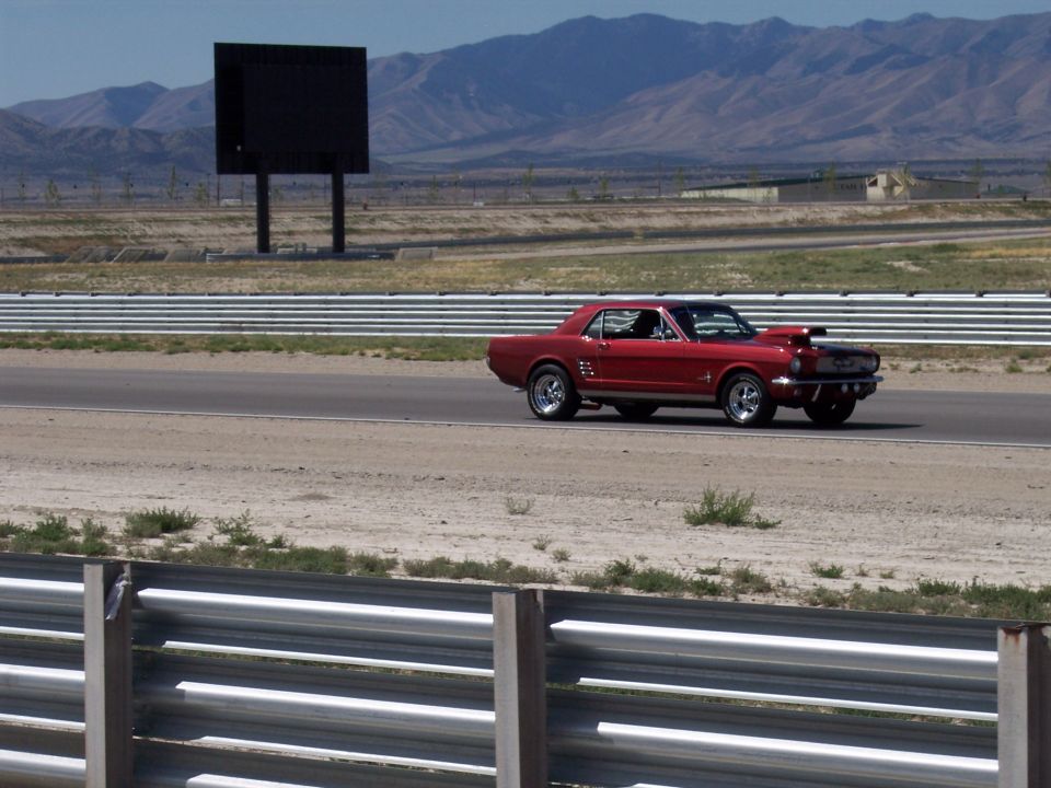 Red classic coupe driving on a racetrack with desert mountains behind