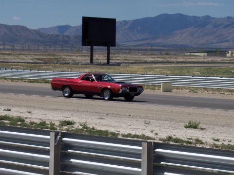 1972 Ford Ranchero - A red 1972 Ford Ranchero drives on a racetrack with mountains in the background.