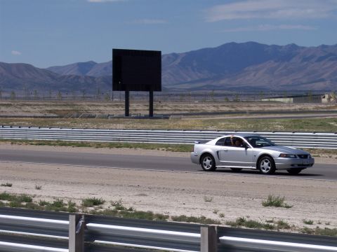 1972 Ford Ranchero - A silver Ford Mustang drives on a track with a large black screen in the distance.