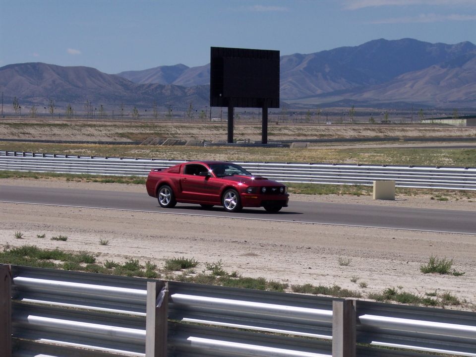 Red Ford Mustang coupe on a racetrack with mountains behind