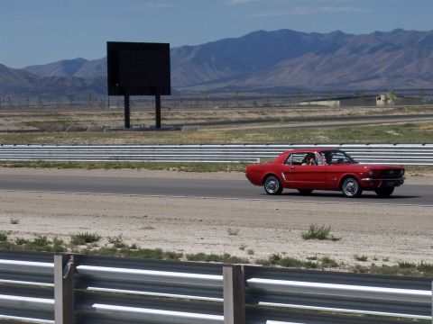 1972 Ford Ranchero - A red 1965 Ford Mustang coupe is seen on a racetrack, with mountains visible in the distance.