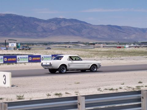 1972 Ford Ranchero - A white 1965 Ford Mustang coupe drives on a racetrack with mountains in the background.