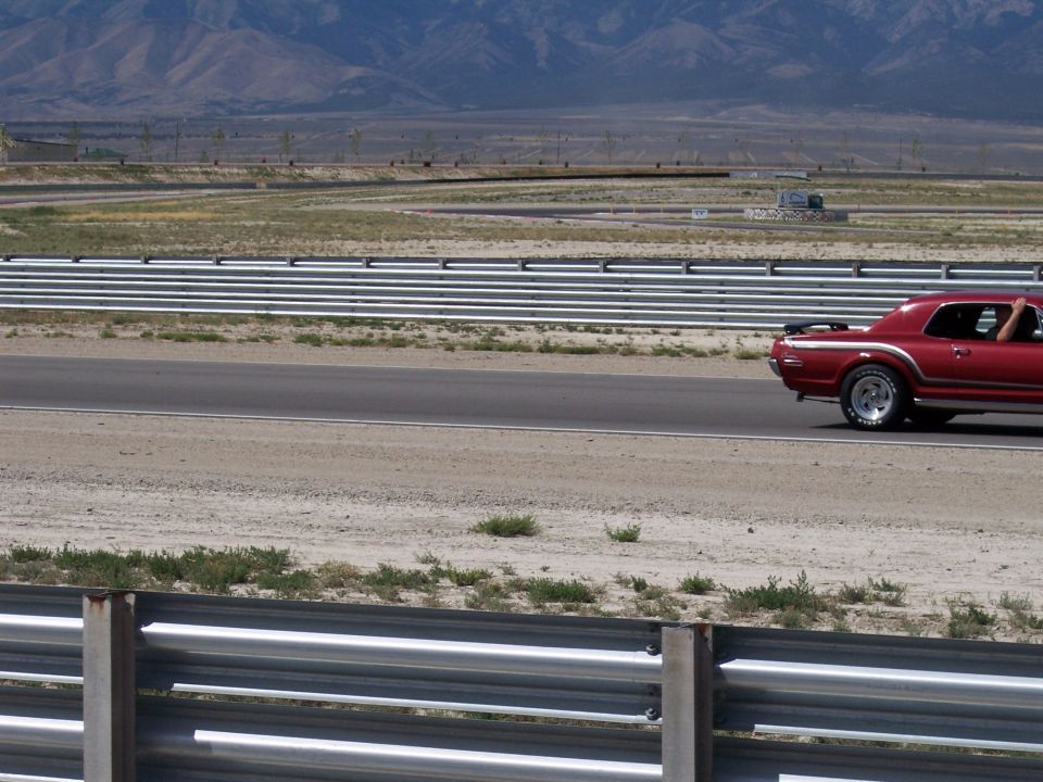 Dark red classic Ford coupe driving on a racetrack with mountains behind