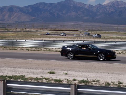 1972 Ford Ranchero - Black Ford Mustang driving on a race track with mountains in the distance.