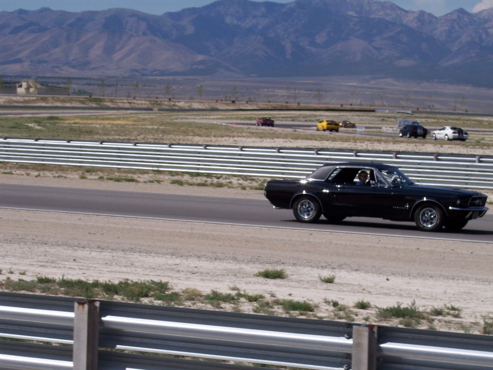 Black classic Mustang coupe driving on a desert racetrack, side view