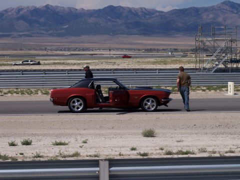 1972 Ford Ranchero - A red coupe with a black roof and open driver's door sits on a track, with mountains in the background.