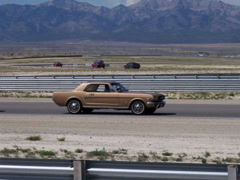 1972 Ford Ranchero - A 1965 Ford Mustang coupe drives on a race track with mountains behind it.