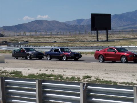 1972 Ford Ranchero - Multiple Ford Mustangs are captured in motion on a paved race track with mountains in the background.