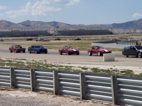 1972 Ford Ranchero - A red 1972 Ford Ranchero leads a group of cars on a race track under a partly cloudy sky.