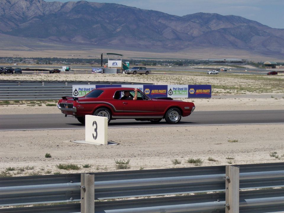 Red coupe driving on a desert race track past a number 3 marker board