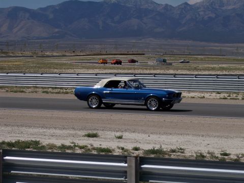 1972 Ford Ranchero - Blue 1968 Ford Mustang convertible driving on a racetrack with mountains in the distance.
