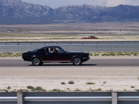 1972 Ford Ranchero - A black 1967 Ford Mustang Fastback is seen on a race track with a red car in the distance.