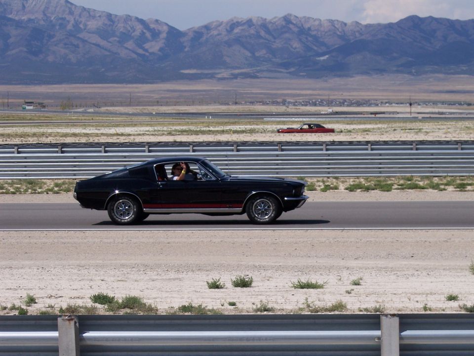 Black Mustang fastback coupe in profile on a desert highway, driver waving