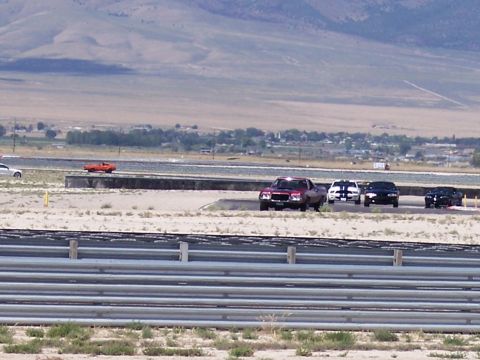 1972 Ford Ranchero - Several cars race on a track with a town and mountains in the background.
