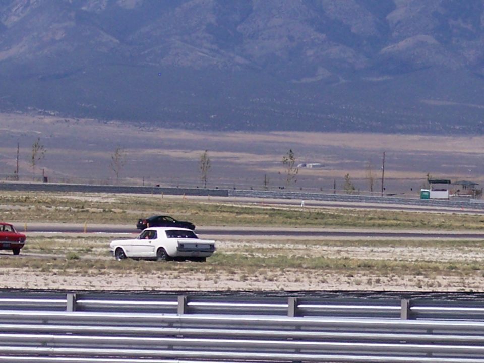 White classic Mustang coupe with black roof on a desert track with mountains behind.