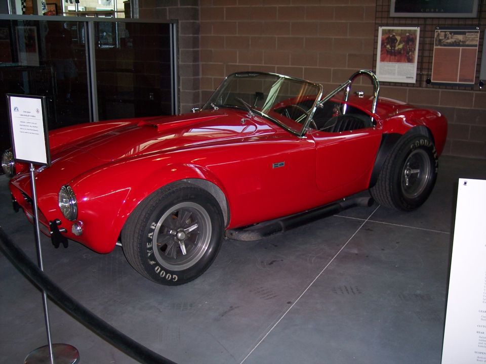 Red Cobra-style roadster on museum display floor, 3/4 front view